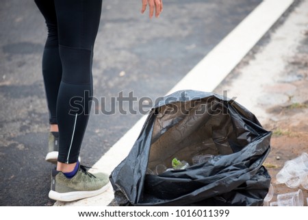 The runner is throwing a glass of plastic into a black garbage bag.