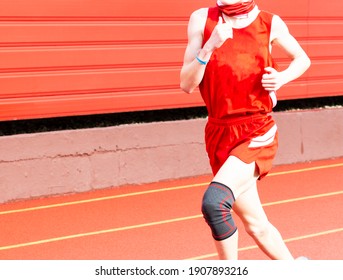 Runner Wearing A Black Knee Brace While Running A Race On A Red Track Next To A Red Wall.