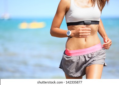 Runner Woman With Heart Rate Monitor Running On Beach With Watch And Sports Bra Top. Beautiful Fit Female Fitness Model Training And Working Out Outside In Summer At Part Of Healthy Lifestyle.