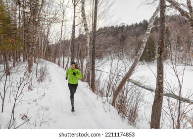 Runner Woman Running Outside In Winter Snow On Cold Winter Day In Forest. Fit Healthy Lifestyle Concept With Beautiful Young Fitness Model. Mixed Race Asian Caucasian Jogging Outside In Full Length