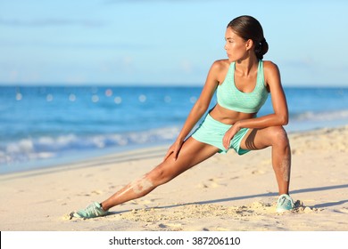 Runner woman stretching legs with lunge hamstring stretch exercise leg stretches. Fitness female athlete relaxing on beach doing a warm-up before her strength training cardio workout.