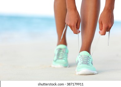 Runner woman tying laces of running shoes preparing for beach jogging. Closeup of hands lacing cross training sneakers trainers for cardio workout. Female athlete living a fit and active life.