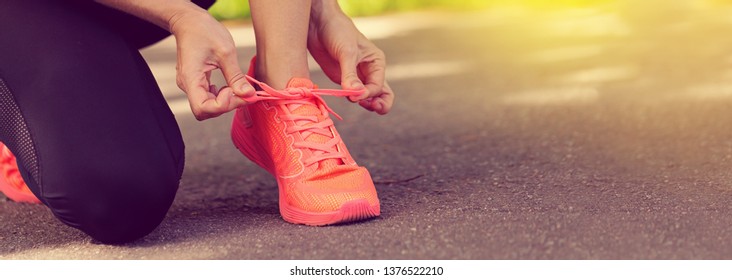 Runner Woman Tying Up Laces Of Shoes, Getting Ready To Run For Cardio And Weight Loss, No Face. Sportive Wear In Trend Colors - Vibrant Coral Neon Color, Long Crop Banner