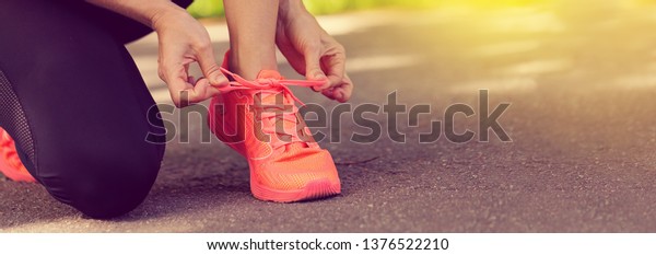 Runner woman tying up laces
of shoes, getting ready to run for cardio and weight loss, no face.
Sportive wear in trend colors - vibrant coral neon color, long crop
banner