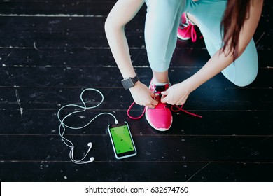 Runner woman tying running shoes laces getting ready for race on run track with smartphone and earphones for music listening on mobile phone. Athlete preparing for cardio training. Feet on ground. - Powered by Shutterstock