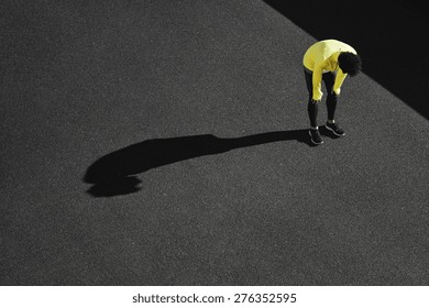 Runner in yellow sportswear resting after running. Jogging man taking a break during training outdoors in on black road on top view. Young Caucasian male fitness model after work out. 