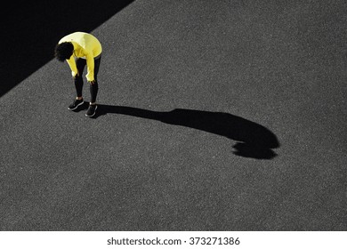 Runner in yellow sportswear resting after running. Jogging man taking a break during training outdoors in on black road on top view. Young Caucasian male fitness model after work out.