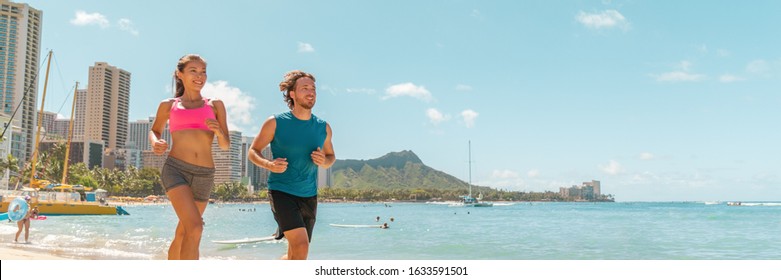 Runners couple running jogging on Hawaii Waikiki beach exercising outdoor in Honolulu city. Active lifestyle banner panoramic landscape background of healthy Asian girl, Caucasian man.