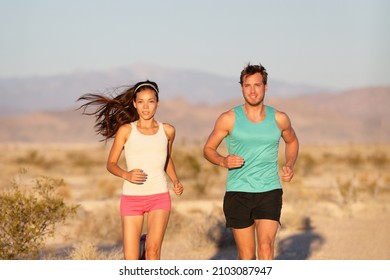 Runners Couple Running Long Distance Ultra Trail Run Race. Runner Man And Sport Woman Training Cardio Outside In Cross Country Sunset Landscape. Fit Male Caucasian Fitness Model, Asian Female Athlete.