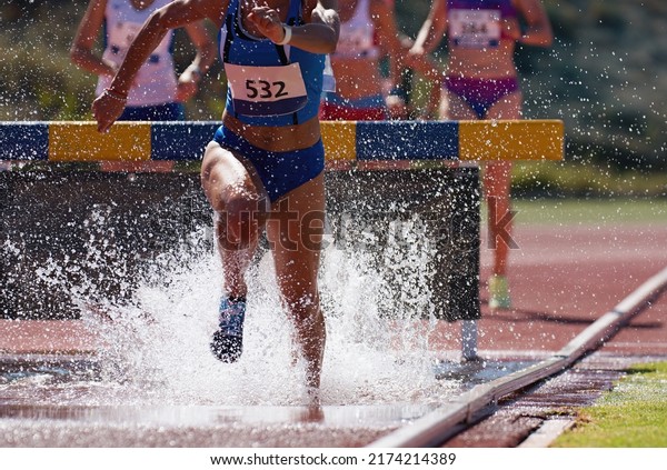 Runners running through the steeplechase water bake\
on a running track, steeplechase females athletes runner overcame\
water jump