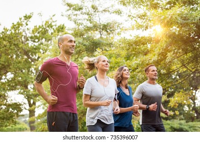 Runners Team On Morning Training Together. Group Of Mature Athletes Running Outside In The Park. Group Of Senior Healthy People Running Outdoor And Doing Fitness Exercises In Summer.