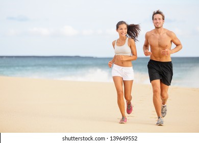 Runners. Young couple running on beach. Athletic attractive people jogging in summer sport shorts enjoying the sun exercising their healthy lifestyle. Multiethnic couple, Asian woman, Caucasian man.