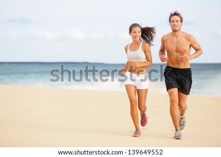Runners. Young couple running on beach. Athletic attractive people jogging in summer sport shorts enjoying the sun exercising their healthy lifestyle. Multiethnic couple, Asian woman, Caucasian man.