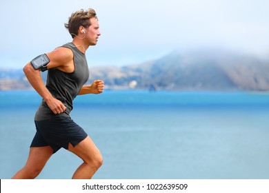 Running app on smartphone. Male runner listening to music jogging with armband for smart phone. Fit man fitness model working outdoor by water.