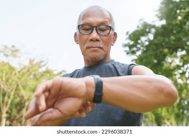Running Asian senior man checking his heartbeat with smartwatch at nature park. Mature Adult male checking pulse after jogging. Fitness tracker - Powered by Shutterstock