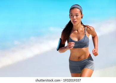 Running athlete woman jogging on beach listening to podcast with wireless earphones and mobile phone. Asian runner doing outdoor exercise healthy active lifestyle. - Powered by Shutterstock