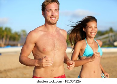 Running Athletic Couple Jogging On Beach Training In Beach Wear Swimsuit, Bikini And Shorts. Shirtless Handsome Man Fitness Model And Beautiful Mixed Race Asian Caucasian Woman Happy And Smiling.