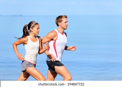 Running couple jogging on beach. Runners training together. Man and woman joggers exercising outdoors. - Powered by Shutterstock