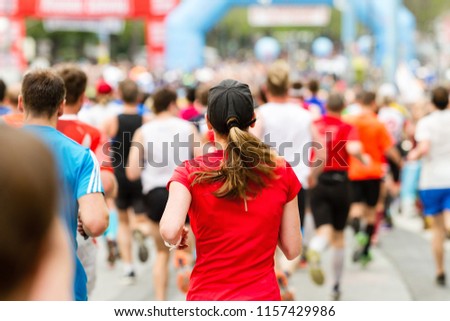 Running crowd at the marathon. Many runners passing the start or finish line. Woman in focus.
