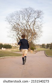 running down a path in the middle of a forest a boy dressed in a suit jacket and shorts with knee-high blue socks
