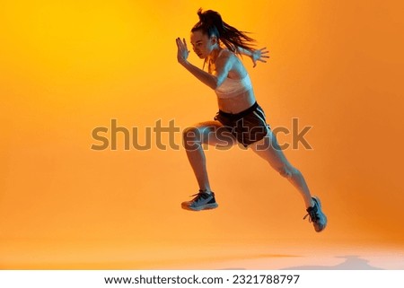 Running. Dynamic image of professional female runner, athlete training over orange studio background in neon light. Concept of sportive lifestyle, health, endurance, action and motion. Ad