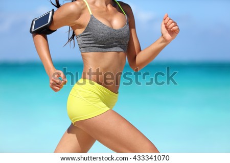 Running fitness woman runner wearing phone armband fast with speed. Hot girl midsection showing muscular legs and motion during intense cardio workout. Woman listening to music over wireless earphones