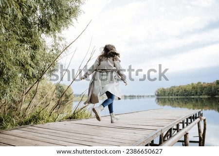 Running girl in clothes in autumn on the bridge, raincoat waving in the wind, loose hair, shoes for walking, gray raincoat. High quality photo