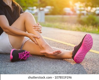 Running injury leg accident- sport woman runner hurting holding painful sprained ankle in pain. Female athlete with joint or muscle soreness and problem feeling ache in her lower body.