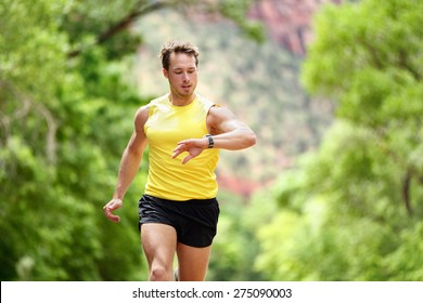 Running Looking At Heart Rate Monitor Smartwatch While Running. Male Runner Jogging Outside Looking At Sports Smart Watch During Workout Training For Marathon Run. Fit Male Fitness Model In His 20s.