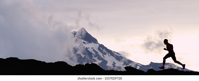 Running Man Athlete Trail Running In Mountain Summit Background. Man On Run Training Outdoors Active Fit Lifestyle. Silhouette At Sunset.