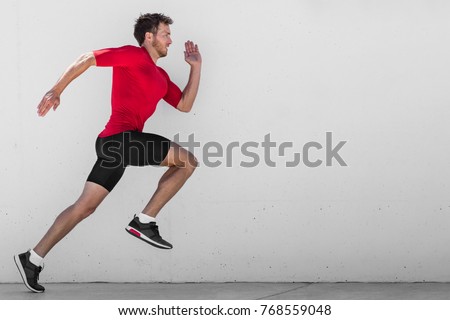 Running man runner training doing outdoor city run sprinting along wall background. Urban healthy active lifestyle. Male athlete doing sprint hiit high intensity interval training.