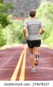 Running Man Runner Working Out For Fitness. Male Athlete On Jogging Run Wearing Sports Running Shoes And Shorts Working Out For Marathon. Full Body Length View Showing Back Running Away.