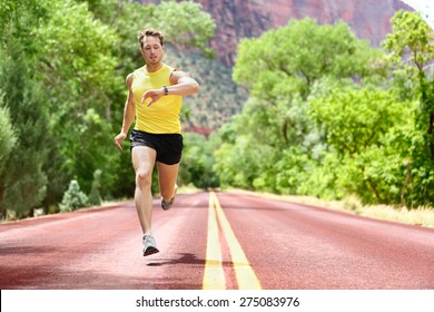 Running Man Sprinting Looking At Heart Rate Monitor Smartwatch On Run. Man Jogging Outside Looking At His Sports Smart Watch During Workout Training For Marathon. Fit Male Fitness Model In His 20s.