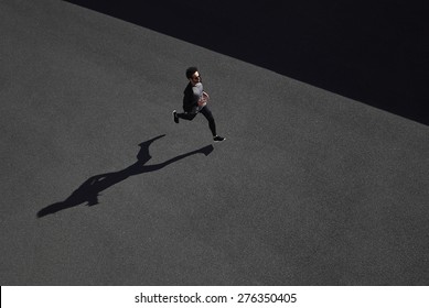 Running Man Sprinting For Success On Run. Top View Athlete Runner Training At Fast Speed At Black Asphalt. Muscular Fit Sport Model Sprinter Exercising Sprint In Yellow Sportswear. 