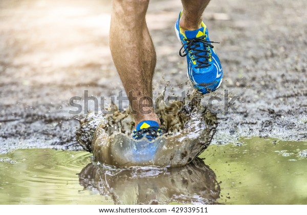 Running man walking in a puddle, splashing\
his shoes. Cross country trail. Freeze\
action