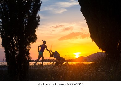 Running Mother With Child In Stroller Enjoying Motherhood At Sunset And Beach Landscape. Jogging Or Power Walking Woman With Pram On A Road At Sunset.