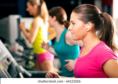 Running On Treadmill In Gym - Group Of Women Exercising To Gain More Fitness, The Woman In Front Wears Earplugs And Enjoys Music