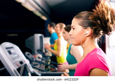 Running On Treadmill In Gym - Group Of Women And Men Exercising To Gain More Fitness, The Woman In Front Wears Earplugs And Enjoys Music