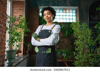 Running of own business. African woman florist wearing apron in botanical store with green plants. Happy small business owner working at flower shop smiling surrounded by plants Small business - Powered by Shutterstock