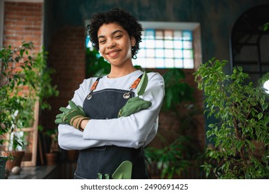 Running of own business. African woman florist wearing apron in botanical store with green plants. Happy small business owner working at flower shop smiling surrounded by plants Small business - Powered by Shutterstock