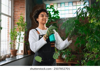 Running of own business. African woman florist with spray bottle watering fertilizing plants in botanical store, Small business owner working at flower shop smiling surrounded by plants Small business - Powered by Shutterstock