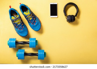 Running Shoes And Fitness Dumbbells In Blue. Blue Gear On A Yellow Background. Fitness With Music. Top.