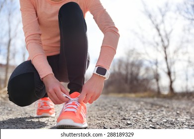 Running Shoes And Runner Sports Smartwatch. Female Runner Tying Shoe Laces On Running Trail Using Smart Watch Heart Rate Monitor.