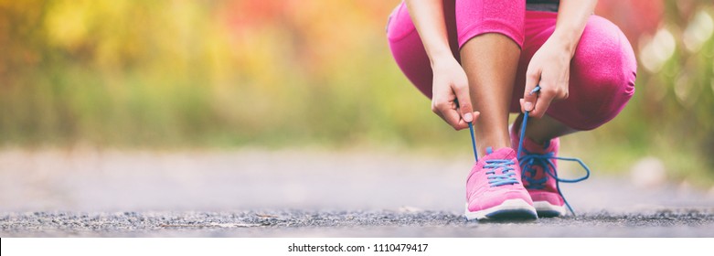 Running shoes runner woman tying laces for autumn run in forest park panoramic banner copy space. Jogging girl exercise motivation heatlh and fitness.