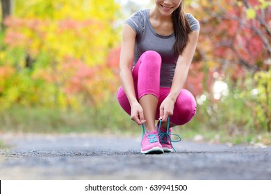 Running Schuhe Frau Läufer binden Schuhspitze für Lauf. Happy lächelnde Mädchen, die sich für die joggings Laktionsschuh Schnürsenkel vorbereitet. Female Sport Fitness Läufer draußen auf Waldweg in Herbst Herbst-Saison.
