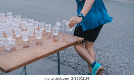 Running, sport, A man is pick up water into cups on a table. The cups are filled with ice and water, and the man is wearing a blue shirt - Powered by Shutterstock