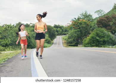 Running Sporty Asian Mom And Daughter. Women Mother And Kid Child Jogging Outdoor On Road Country At Ratchaburi, Thailand. Sports And Fitness Family. Sport And Healthy Concept