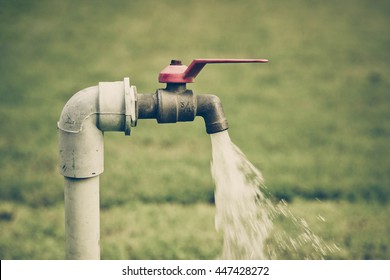 Running water from a tap with green grass background / Water consumption and usage concept