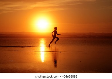 Running woman athlete silhouette at ocean line with sunset (full sun). With feet splashing water & track in the water - Powered by Shutterstock