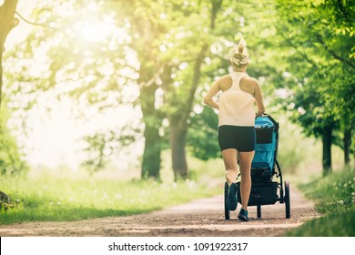 Running woman with baby stroller enjoying summer day in park. Jogging or power walking supermom, active family with baby jogger.